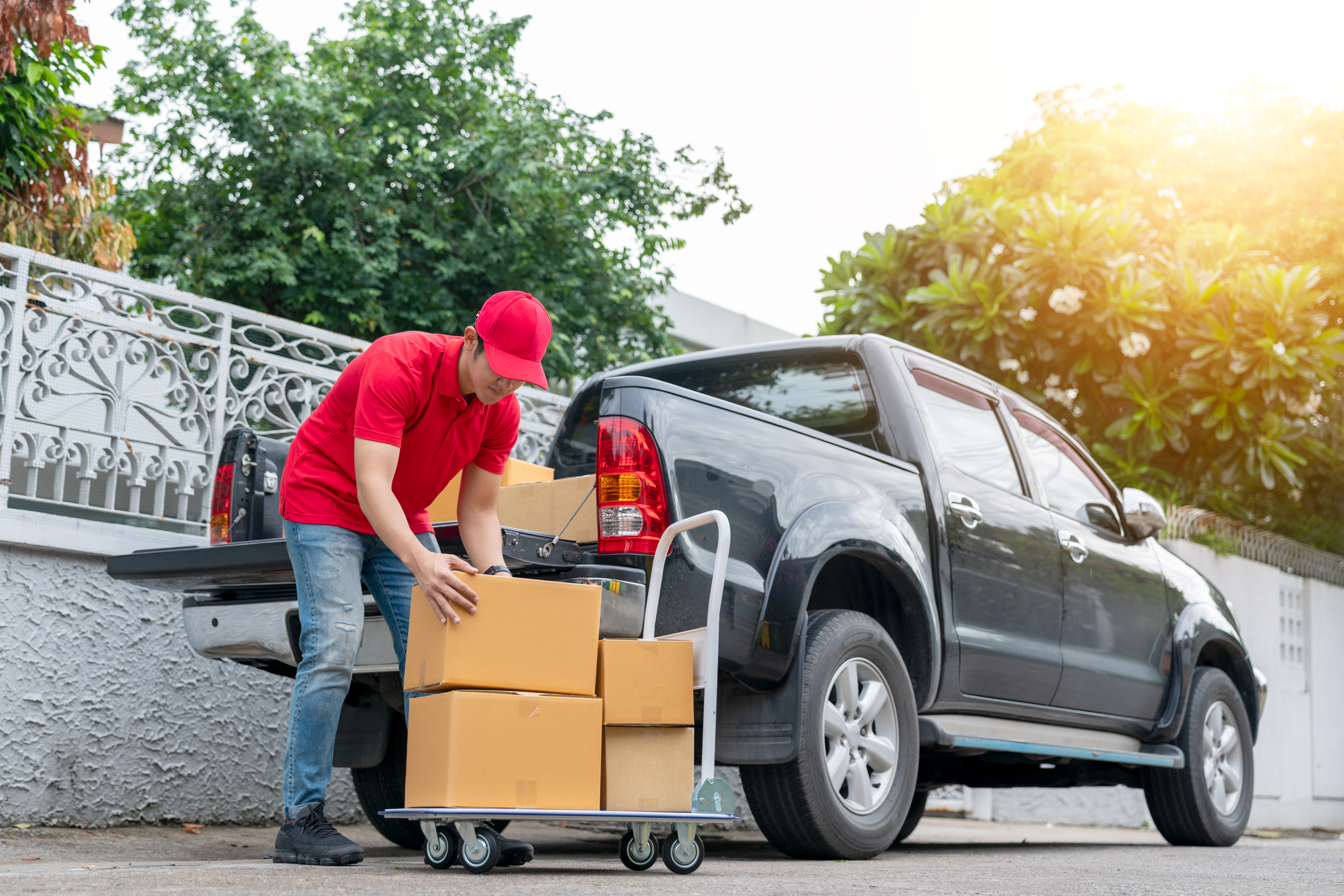 Delivery men in red uniform unloading cardboard boxes from pickup truck. Courier man sending the parcel or package to the customer on a business day. Online shopping and transport logistics concept.